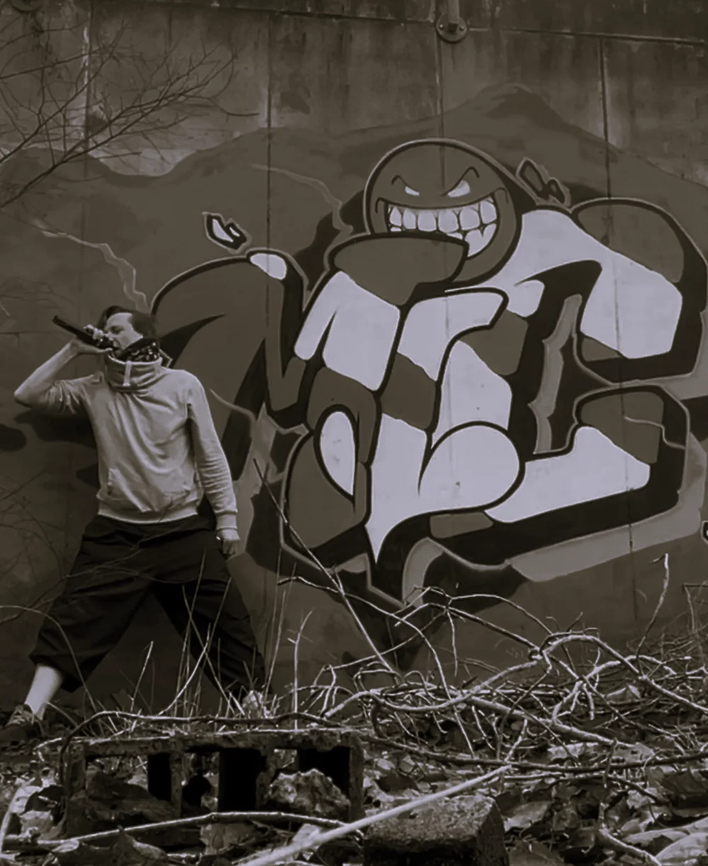 Felipe mit Mikrofon und Halstuch vor dem Gesicht, vor einer Wand mit einem großen Graffiti